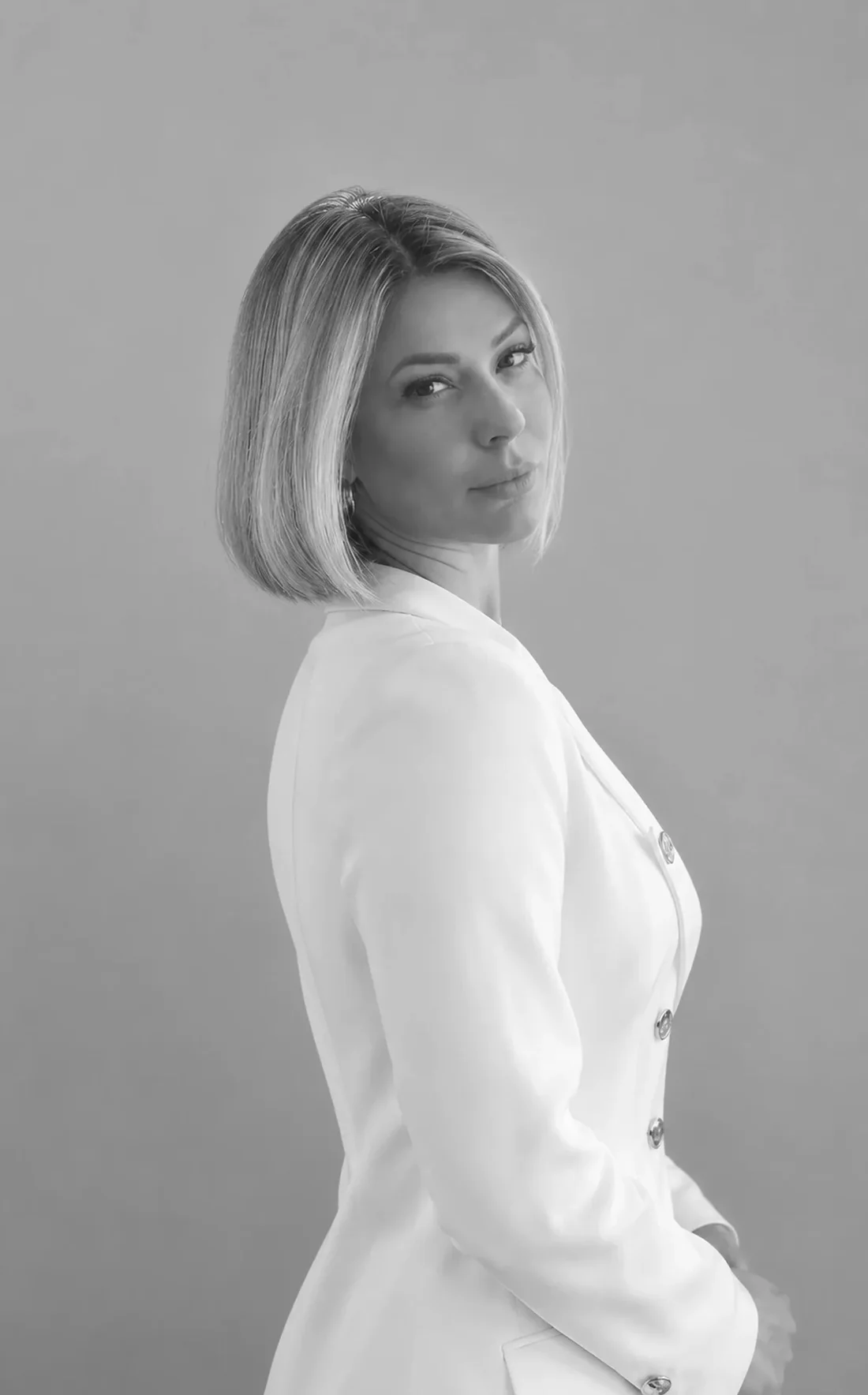 Dra. Marina Raposo de blazer branco, de perfil, com o rosto virado para a câmera, em preto e branco